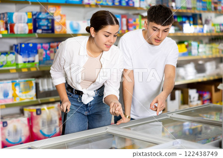 Young couple looking to buy frozen food in supermarket Young couple looking to buy frozen food in supermarket 122438749