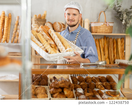 Portrait of smiling baker with fresh bread and baguettes at bakery Portrait of smiling baker with fresh bread and baguettes at bakery 122438750