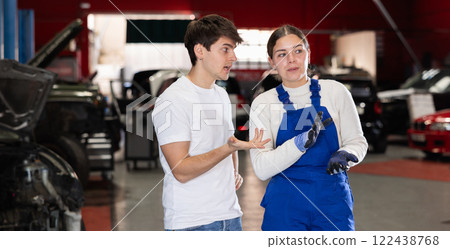 Male client talking to female mechanic in uniform about repairing his car engine in auto repair shop 122438768