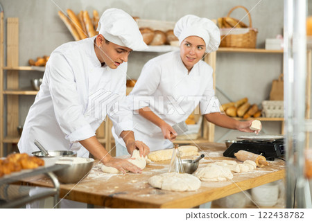 Young male baker kneading dough and girl cutting and weighing small pieces 122438782