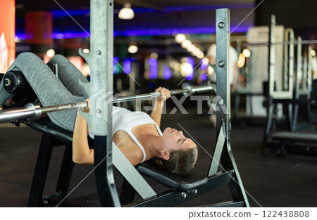 Girl lies on bench and lifts barbell, strengthens muscles of upper body 122438808