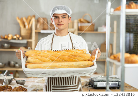 Young male baker holding baguettes in wicker basket 122438816