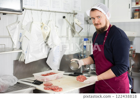 Male food company employee prepares raw meat cutlets using special equipment 122438818