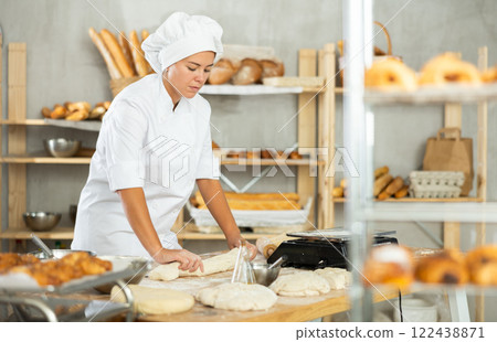 Young female baker shaping dough into baguette in bakery Young female baker shaping dough into baguette in bakery 122438871