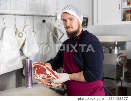 Butcher holding slab of beef rib steaks in shop processing room Butcher holding slab of beef rib steaks in shop processing room 122438877