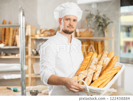 Male bakery employee offering different baguettes for sale Male bakery employee offering different baguettes for sale 122438884