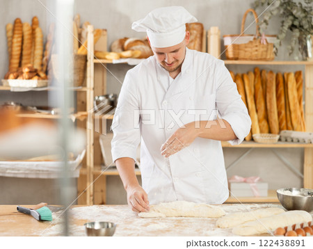 Guy works as baker in bakery, molds sausages from dough, rolls long round strips from dough Guy works as baker in bakery, molds sausages from dough, rolls long round strips from dough 122438891