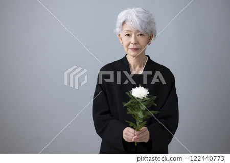 Senior woman wearing mourning clothes and holding chrysanthemum flowers 122440773
