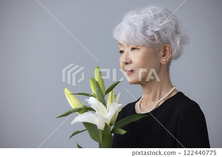 Senior woman wearing mourning clothes and holding a lily flower 122440775