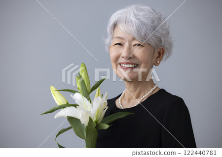 Senior woman wearing mourning clothes and holding a lily flower Senior woman wearing mourning clothes and holding a lily flower 122440781