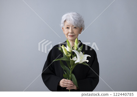 Senior woman wearing mourning clothes and holding a lily flower Senior woman wearing mourning clothes and holding a lily flower 122440785