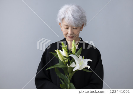 Senior woman wearing mourning clothes and holding a lily flower 122441001