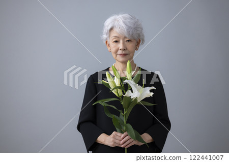 Senior woman wearing mourning clothes and holding a lily flower 122441007