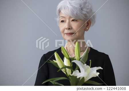 Senior woman wearing mourning clothes and holding a lily flower 122441008