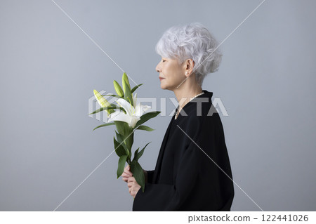 Senior woman wearing mourning clothes and holding a lily flower 122441026