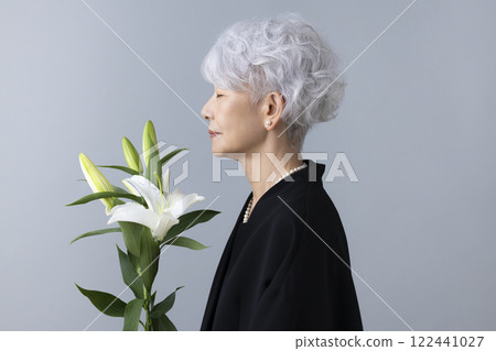 Senior woman wearing mourning clothes and holding a lily flower Senior woman wearing mourning clothes and holding a lily flower 122441027