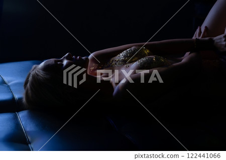 Woman in gold attire relaxing on a dark surface during a low-light setting 122441066