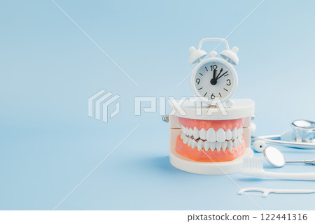 A Dentist presents a teeth model with a white alarm clock, emphasizing oral care, dentistry tools 122441316