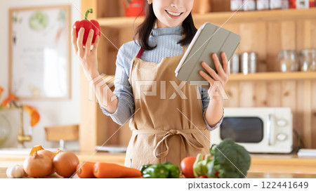 A smiling woman cooking while looking at a tablet 122441649