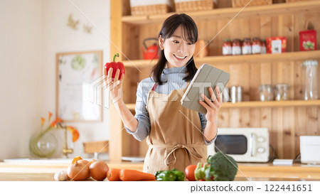 A smiling woman cooking while looking at a tablet 122441651