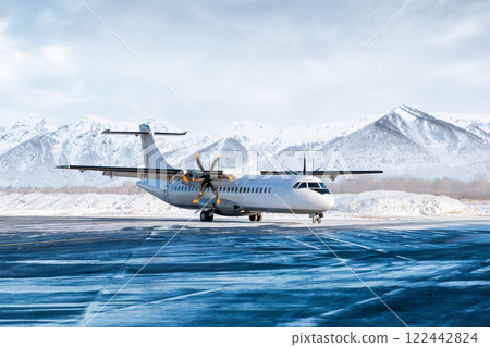 White passenger turboprop airliner on the winter airport apron on the background of high picturesque mountains 122442824