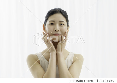 一位微笑的年輕女子，穿著背心，背景為白色，雙手托住臉頰 122445559