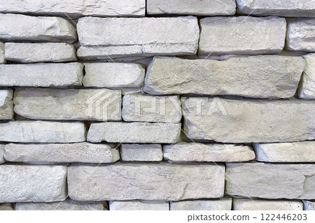 Textured Stone Wall Background.A close-up view of a textured stone wall. The wall is constructed from irregularly shaped, light-colored stones that are stacked in a horizontal pattern. 122446203