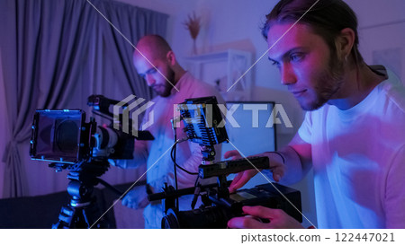 Cameraman backstage. Behind scene. Male videographer looks digital display while filming. Photo crew works in half dark pro studio. Cameraman backstage. Behind scene. Male videographer looks digital display while filming. Photo crew works in half dark pro studio. 122447021