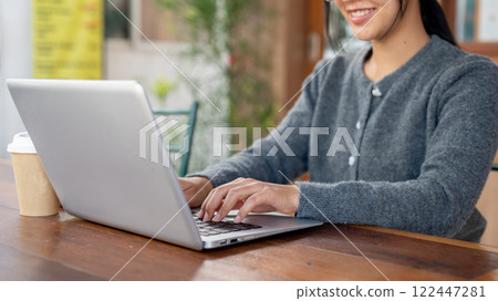 A close-up of a woman works on her laptop while sitting in a cafe. 122447281