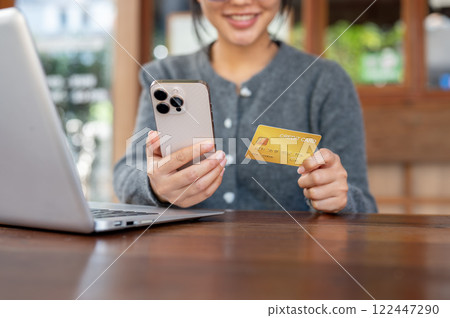 A close-up of happy Asian woman shops online on her smartphone while sitting in a cafe. A close-up of happy Asian woman shops online on her smartphone while sitting in a cafe. 122447290