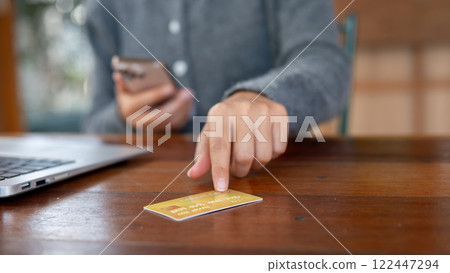 A close-up of a woman pointing at a credit card on a table, shopping online, online payment. A close-up of a woman pointing at a credit card on a table, shopping online, online payment. 122447294