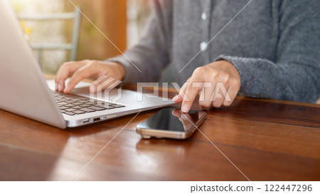 A close-up of a woman pointing at a smartphone on a table, working remotely at a coffee shop. A close-up of a woman pointing at a smartphone on a table, working remotely at a coffee shop. 122447296