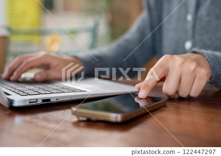 A close-up of a woman pointing at a smartphone on a table, working remotely at a coffee shop. 122447297