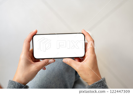 A top view of a woman holds a smartphone in a horizontal positive as she watching videos, indoors. 122447309