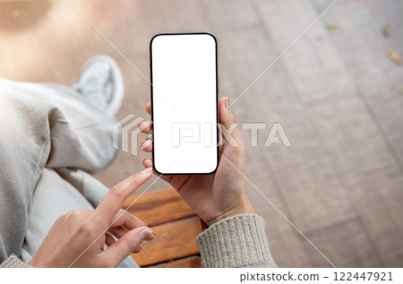 Top view of a woman uses her phone while sitting indoors. the smartphone with a white screen mockup 122447921