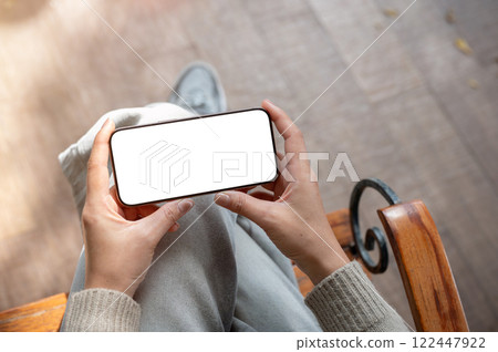 A top view of a woman sits indoors and holds her smartphone in a horizontal position. A top view of a woman sits indoors and holds her smartphone in a horizontal position. 122447922
