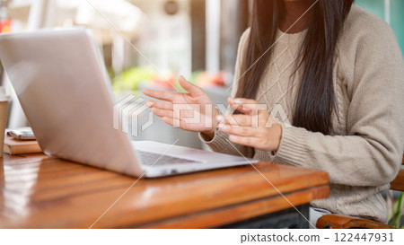 A close-up of a woman talking on an online meeting through her laptop, working remotely from a cafe. 122447931