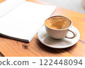 Open Blank Book and Cappuccino on Wooden Table in Cozy Cafe 122448094
