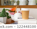 Takeaway Coffee Cup on a Cozy Table with Teapot and Plants 122448100