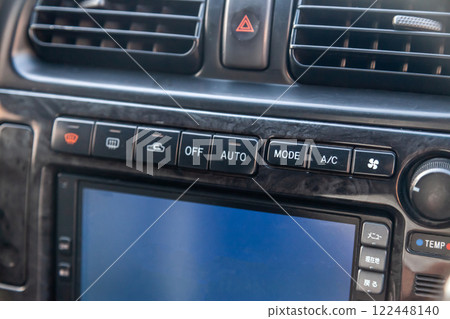 Close-up of the center console on a gray panel inside the car, with climate control and a red emergency button. Setting up and refueling the air conditioner in the workshop. 122448140