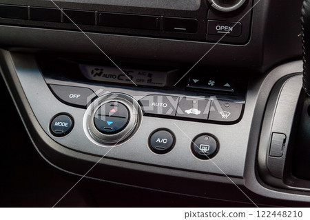 Close-up of the center console on a gray panel inside the car, with climate control and a red emergency button. Setting up and refueling the air conditioner in the workshop. 122448210