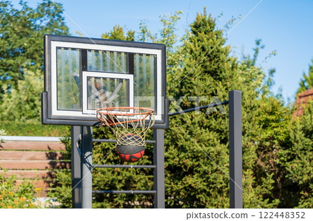 Basketball hoop with ball in outdoor setting surrounded by greenery on a sunny day Basketball hoop with ball in outdoor setting surrounded by greenery on a sunny day 122448352