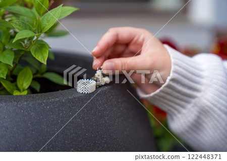Female hand holding beaded jewelry near green plant in minimalist setting 122448371