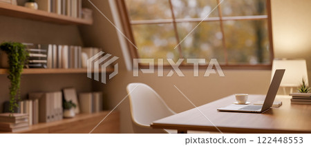 A laptop on a hardwood desk in a cozy, contemporary office, illuminated by a lamp. A laptop on a hardwood desk in a cozy, contemporary office, illuminated by a lamp. 122448553