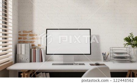 A computer and decorative items placed on a white desk against a white brick wall. 122448562