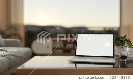 A laptop with a white screen mockup placed on a modern coffee table in a contemporary living room. A laptop with a white screen mockup placed on a modern coffee table in a contemporary living room. 122448580