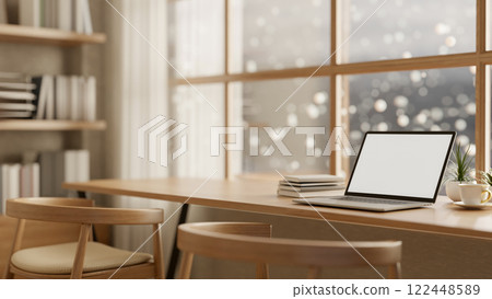 A laptop on a wooden table, positioned by a window with a snowy view, set in a cozy, minimalist room 122448589