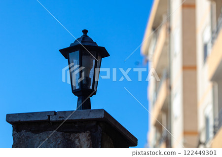Small lamp lamp on a stone pillar. In the background a tree and blue sea. High quality photo. Small lamp lamp on a stone pillar. In the background a tree and blue sea. High quality photo. 122449301