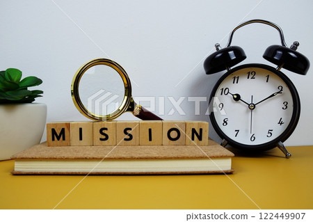 Magnifying glass and alarm clock with wooden blocks alphabet letters MISSION text message on yellow background 122449907