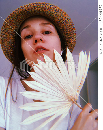 Vertical female portrait of a young woman, girl wearing a straw hat with a dry palm branch in a hand in summer. Summertime vacation travel, lifestyle. 122449972